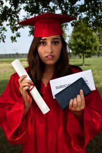 Graduate holding diploma, checkbook and student loan bill. This is a conceptual image about student loans and debt.